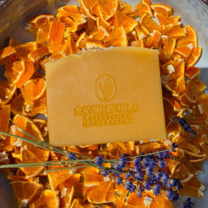 Orangene Seife liegend in Orangenschalenstücken und Lavendelstrauß