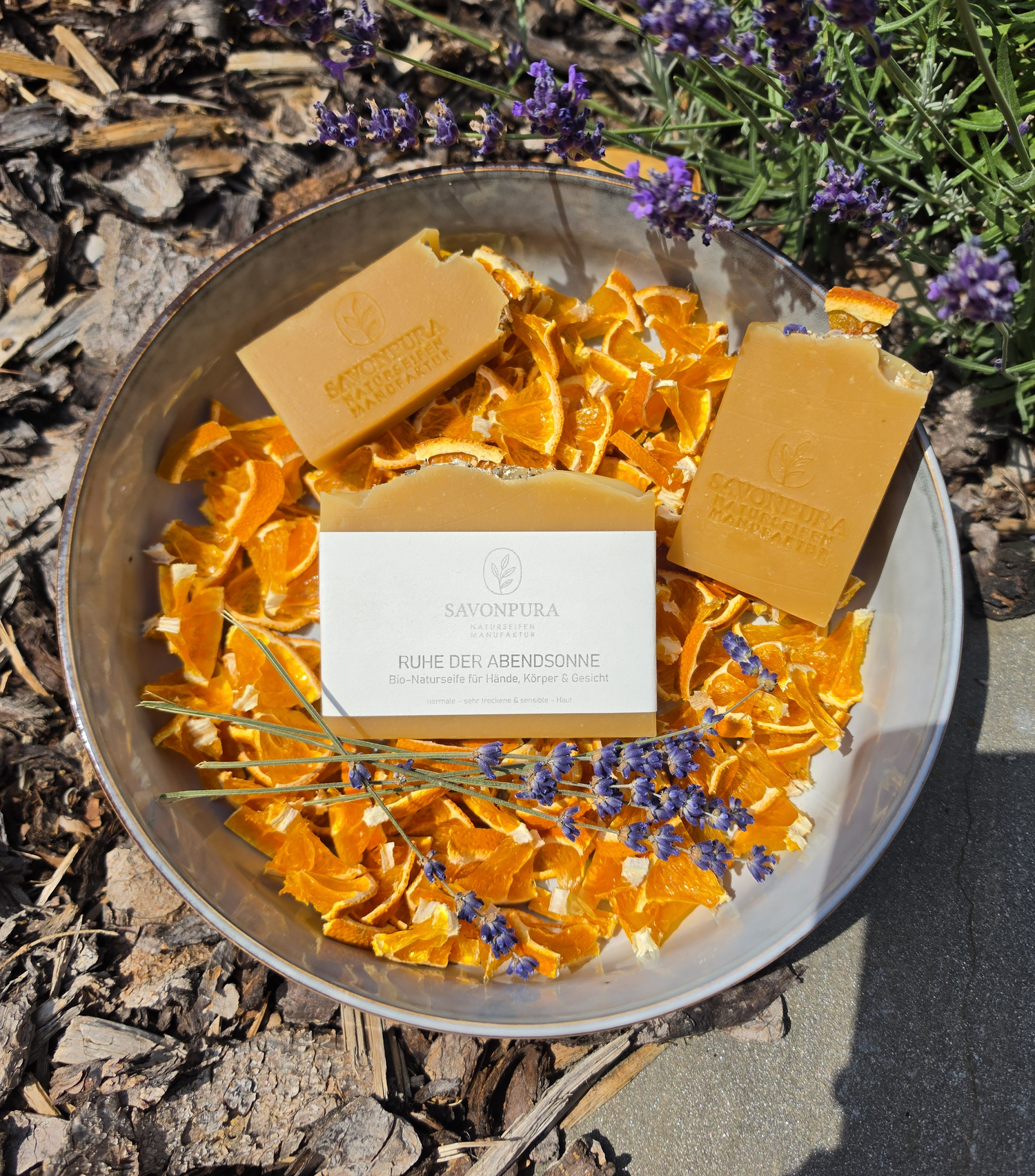 Seife mit Etikett mit 2 kleineren in Schüssel mit Orangenscheibenstückchen und Lavendel mit Naturdeko