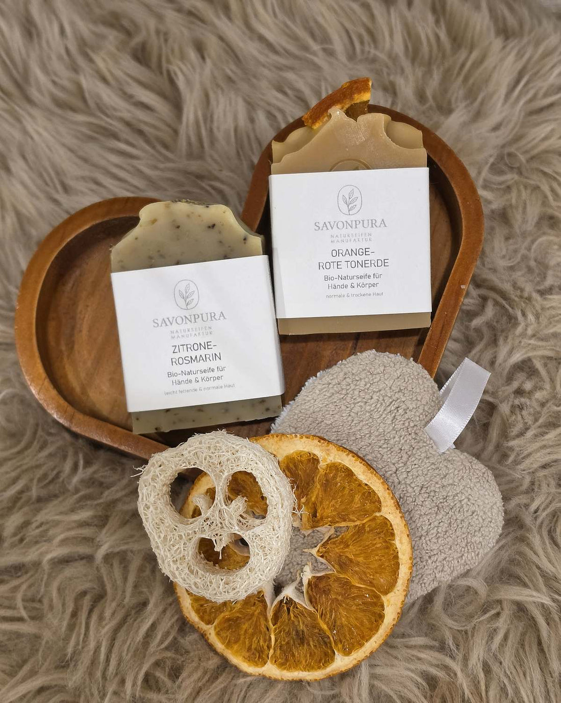 2 Seifen je 60g in Holzherz auf beigem Fell liegend. Orange-Rote Tonerde und Zitrone-Rosmarin. Mit Etikett &amp; Naturdeko. Orangenscheibe.